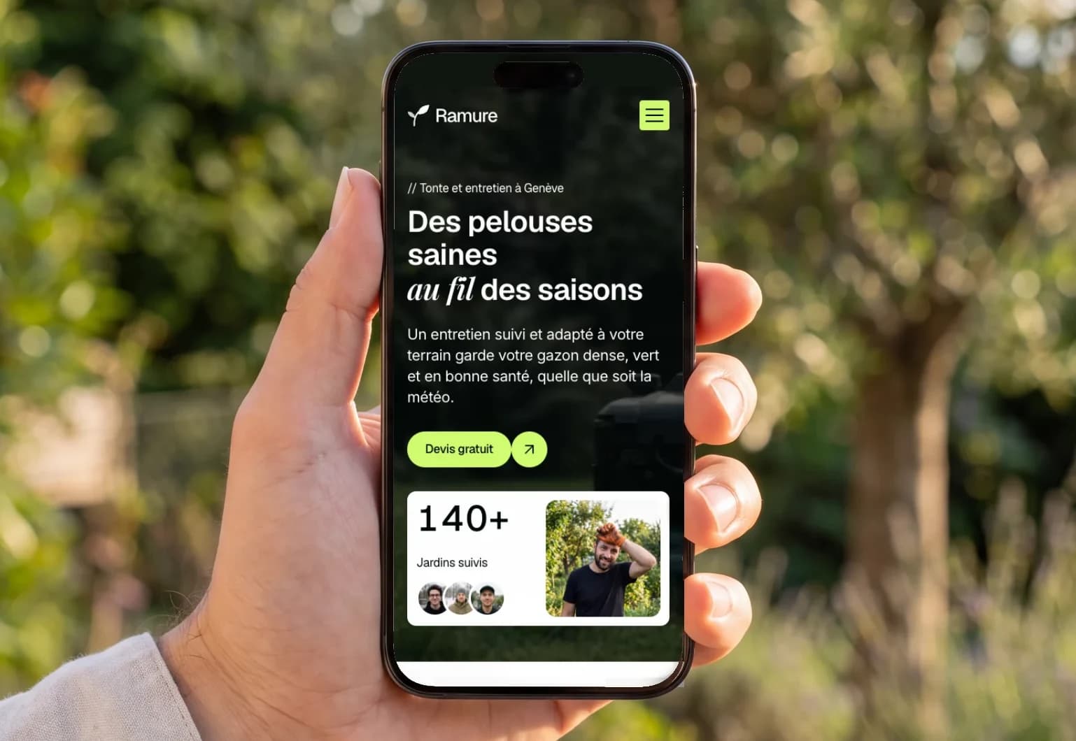 La démo Ramure, site d’un paysagiste genevois, affichée sur un téléphone tenu en main dans un jardin ensoleillé